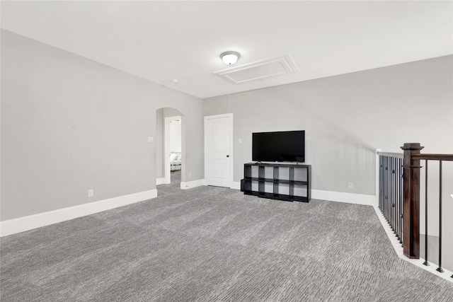 unfurnished living room featuring attic access, arched walkways, carpet flooring, and baseboards