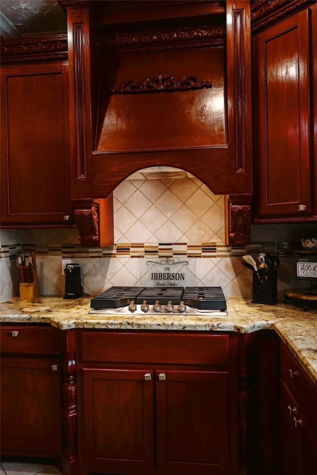 kitchen featuring reddish brown cabinets, stainless steel gas cooktop, decorative backsplash, and light stone countertops