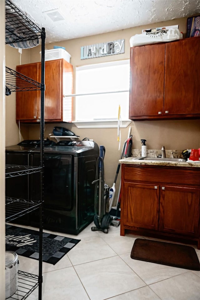 clothes washing area featuring cabinet space, a textured ceiling, washing machine and dryer, a sink, and light tile patterned flooring