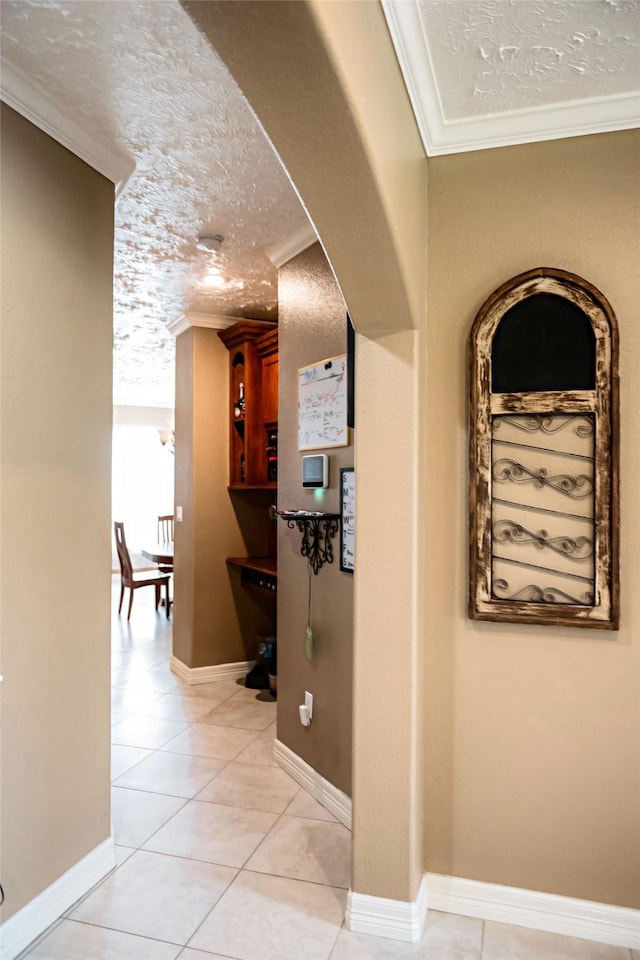 hallway featuring light tile patterned floors, a textured ceiling, baseboards, and crown molding