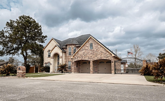 french provincial home with a garage, concrete driveway, a gate, fence, and brick siding