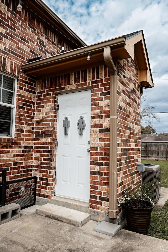 doorway to property featuring a garage, brick siding, cooling unit, and fence