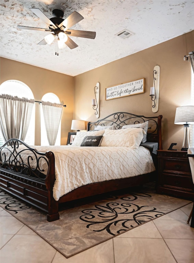 bedroom featuring a textured ceiling, a ceiling fan, visible vents, and tile patterned floors