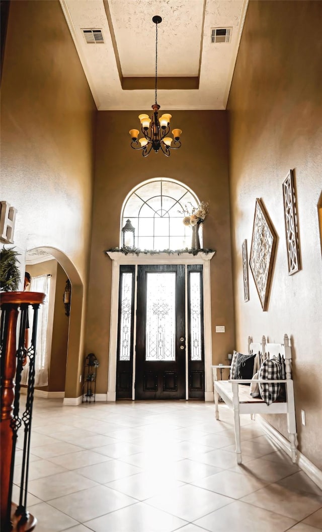 tiled foyer entrance with visible vents, arched walkways, a high ceiling, a tray ceiling, and a chandelier