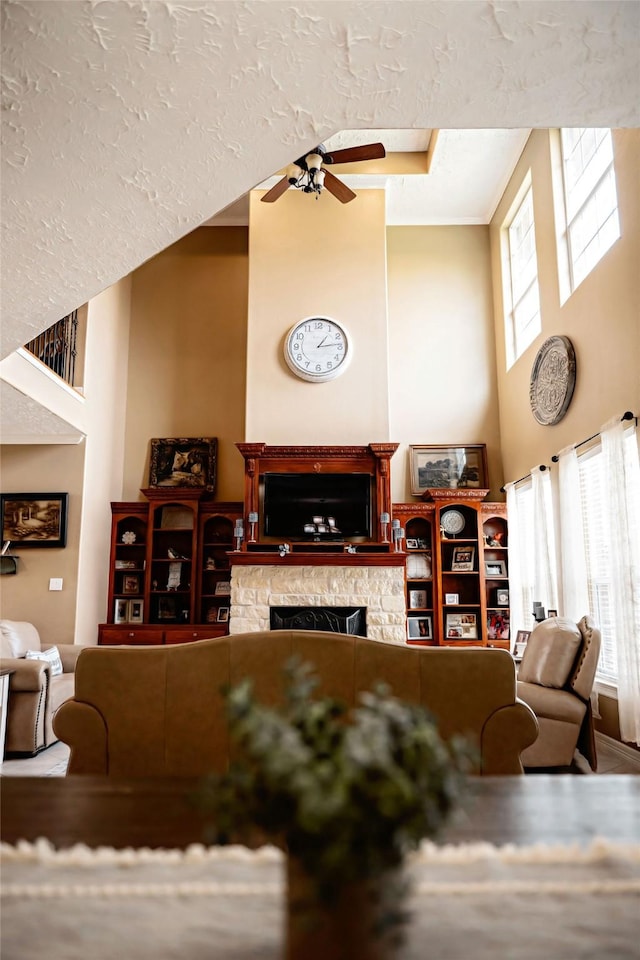 living room with a towering ceiling, ceiling fan, a fireplace, and a textured ceiling