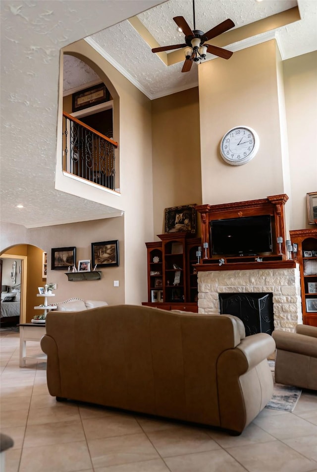 living room featuring tile patterned flooring, ceiling fan, a stone fireplace, and a textured ceiling