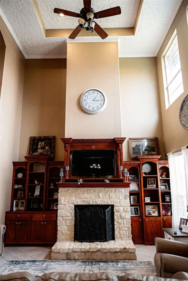 living area featuring tile patterned floors, ceiling fan, a textured ceiling, and a stone fireplace