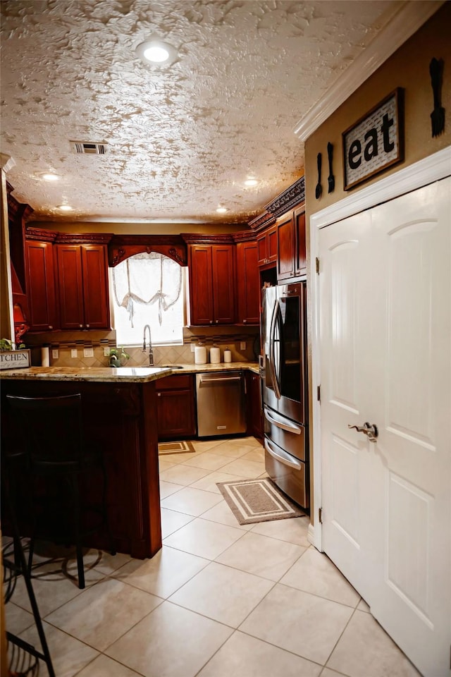 kitchen with reddish brown cabinets, visible vents, appliances with stainless steel finishes, light stone counters, and a sink