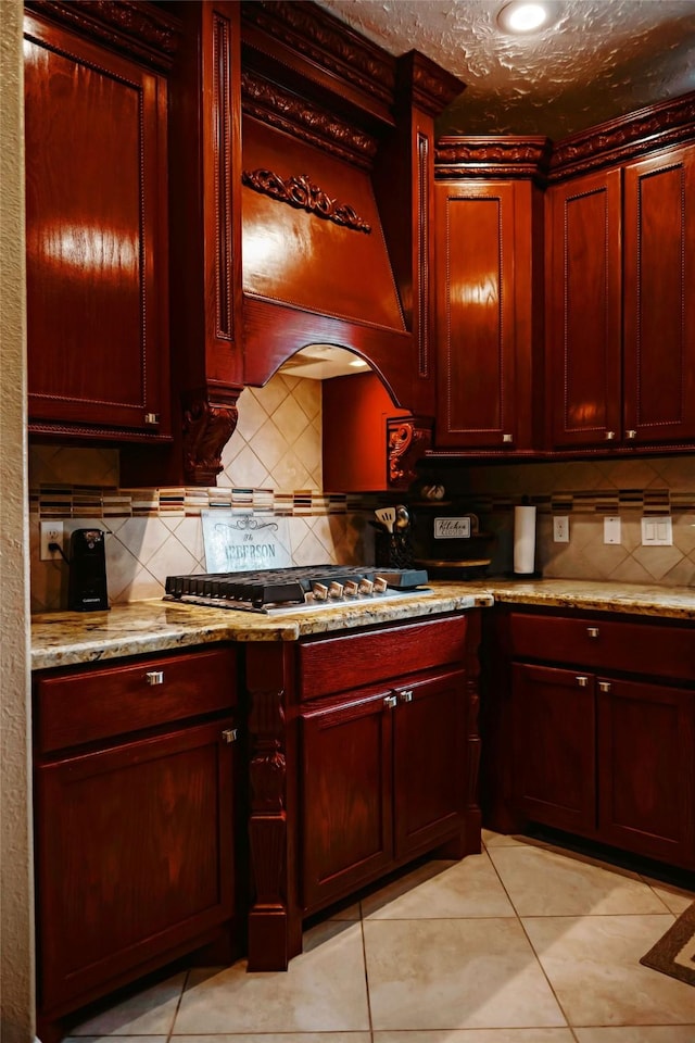 kitchen with reddish brown cabinets, light stone counters, decorative backsplash, and stainless steel gas cooktop