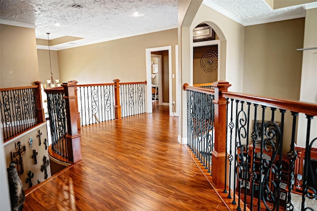 corridor with visible vents, ornamental molding, a textured ceiling, an upstairs landing, and wood finished floors