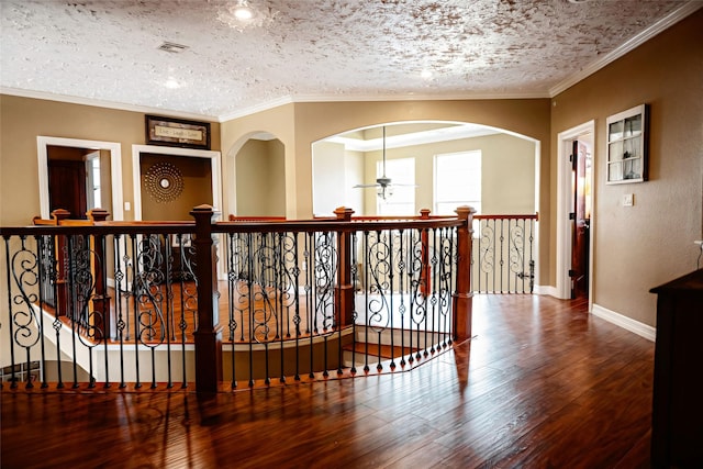 corridor with baseboards, visible vents, wood finished floors, crown molding, and a textured ceiling