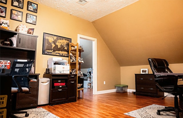 home office with lofted ceiling, visible vents, a textured ceiling, wood finished floors, and baseboards