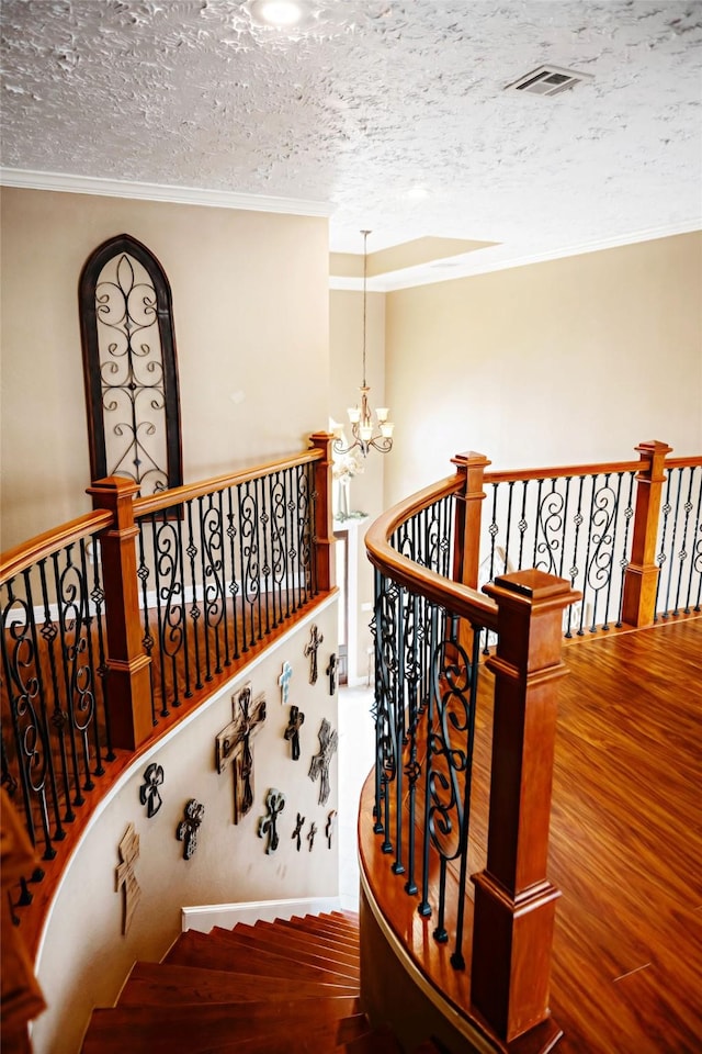 stairs with crown molding, an inviting chandelier, and wood finished floors