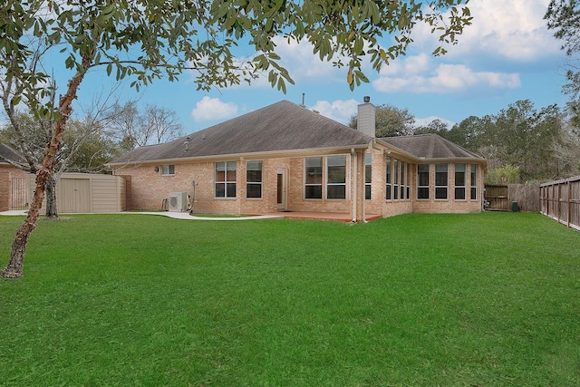 back of house featuring a fenced backyard, a lawn, a chimney, and brick siding