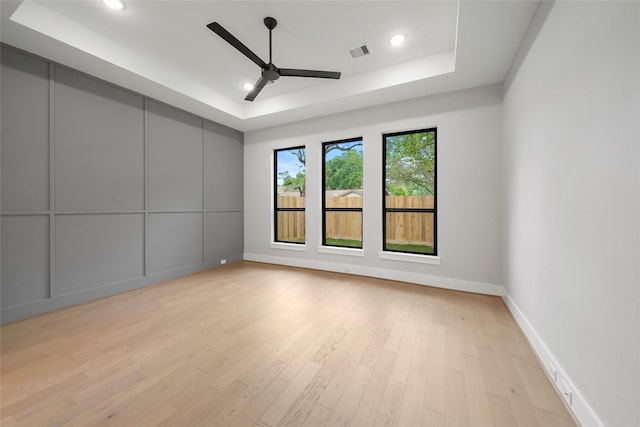 unfurnished room with light wood-style floors, a ceiling fan, visible vents, and a tray ceiling