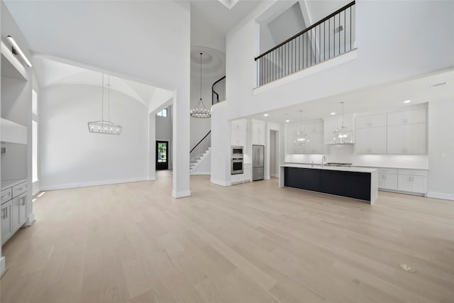 unfurnished living room with a chandelier, a towering ceiling, baseboards, light wood-style floors, and stairway