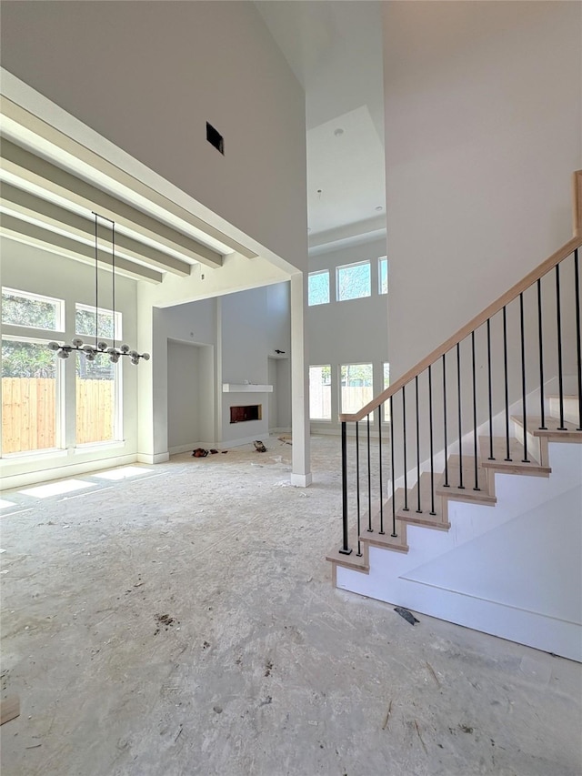 unfurnished living room featuring an inviting chandelier, stairs, a fireplace, and a towering ceiling