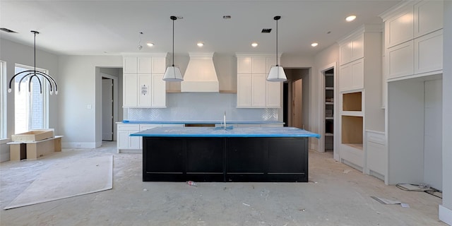 kitchen with tasteful backsplash, white cabinets, recessed lighting, custom exhaust hood, and a center island with sink