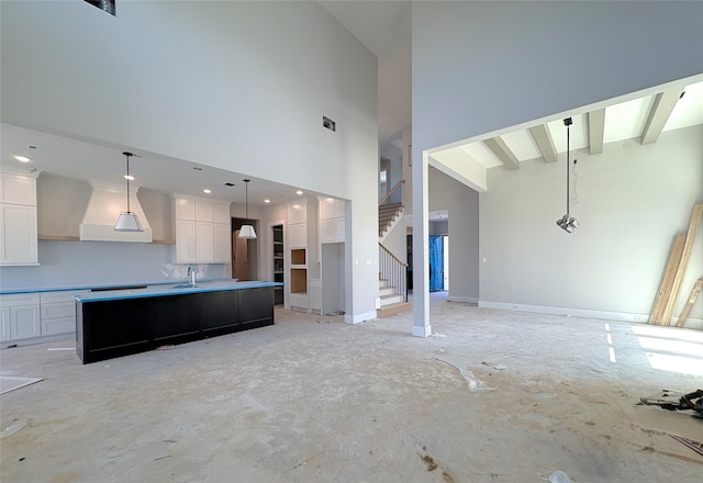 unfurnished living room featuring a towering ceiling, stairs, a sink, and baseboards