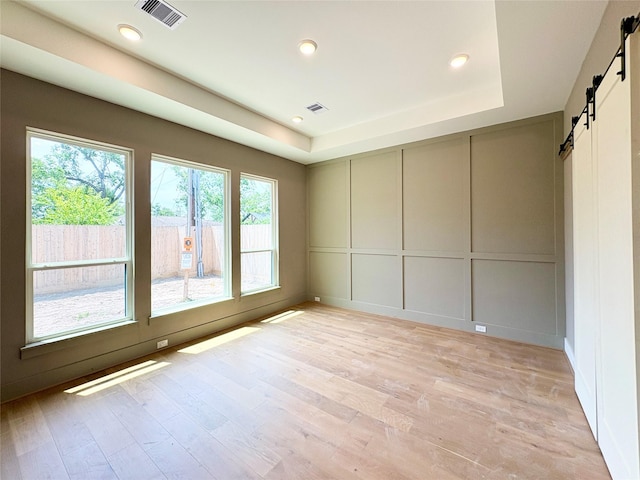 1953 Coulcrest Dr, Houston, TX 77055 - unfurnished room featuring a barn door, a decorative wall, a raised ceiling, light wood-style flooring, and recessed lighting