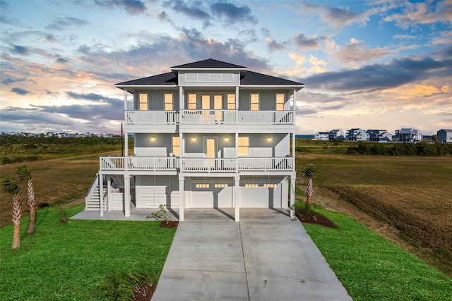 beach home with a balcony, a garage, stairs, driveway, and a front lawn