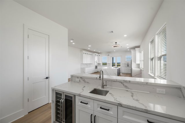 kitchen with light wood finished floors, visible vents, wine cooler, white cabinetry, and a sink