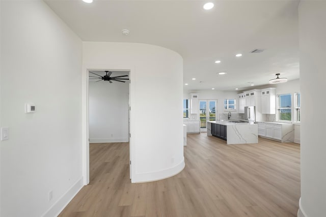 kitchen featuring a kitchen island with sink, white cabinets, light countertops, and light wood-style flooring