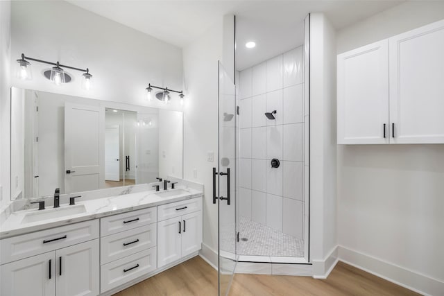 full bath featuring double vanity, wood finished floors, a stall shower, and a sink