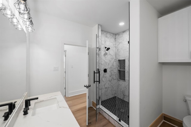 full bathroom with a marble finish shower, toilet, vanity, wood finished floors, and baseboards