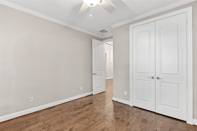 unfurnished bedroom featuring wood-type flooring, visible vents, a closet, ornamental molding, and baseboards