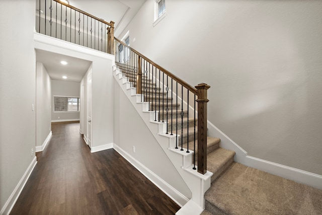 staircase with a high ceiling, baseboards, and wood finished floors