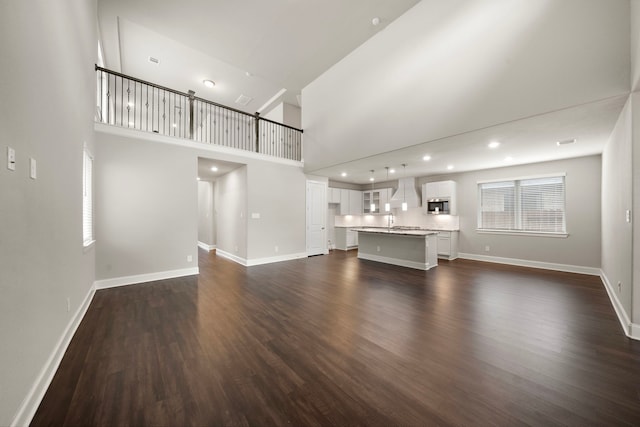 unfurnished living room with dark wood-style floors, a high ceiling, and baseboards