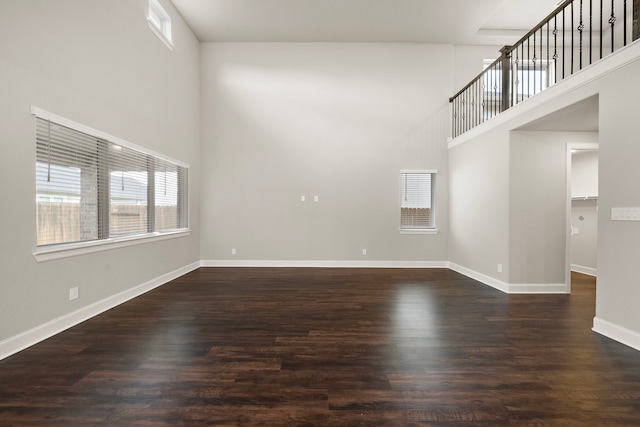 empty room featuring dark wood-style flooring, a high ceiling, and baseboards