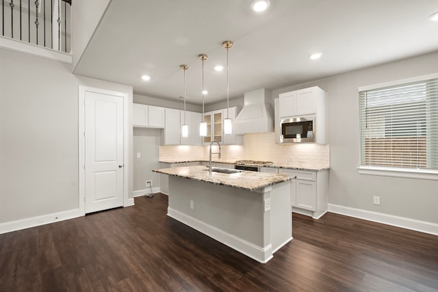 kitchen with a sink, light stone countertops, dark wood-style floors, stainless steel microwave, and custom range hood