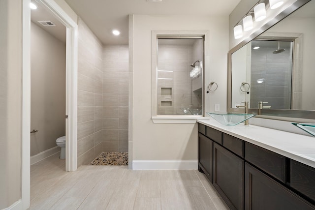 full bathroom with visible vents, toilet, vanity, tiled shower, and baseboards