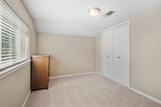 unfurnished bedroom with baseboards, visible vents, lofted ceiling, carpet, and a textured ceiling