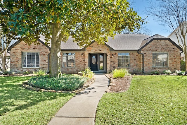 view of front of house featuring brick siding, a shingled roof, and a front yard