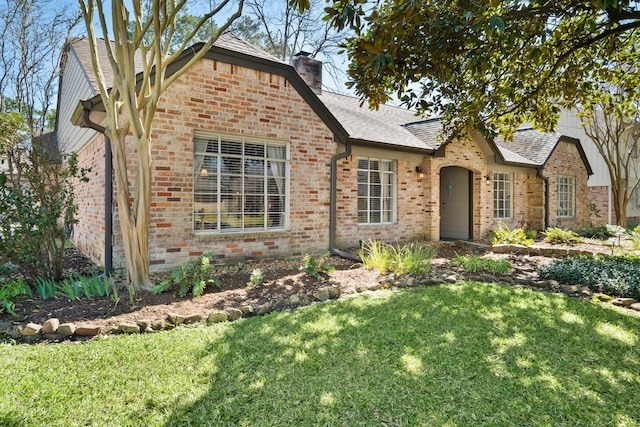 view of front of house featuring brick siding, a chimney, a front yard, and a shingled roof