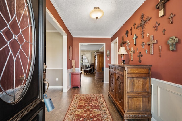 foyer entrance with a textured ceiling, ornamental molding, dark wood-style flooring, and wainscoting