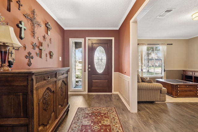 foyer with visible vents, wainscoting, wood finished floors, crown molding, and a textured ceiling