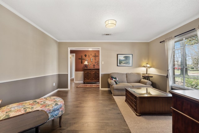 living area with a textured ceiling, ornamental molding, wood finished floors, and visible vents