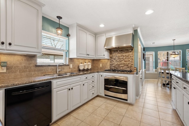 kitchen with stainless steel appliances, wall chimney range hood, a sink, and pendant lighting