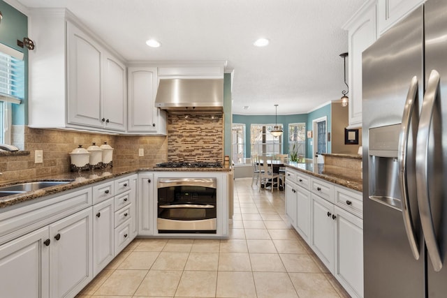 kitchen with light tile patterned floors, stainless steel appliances, white cabinets, decorative backsplash, and wall chimney exhaust hood