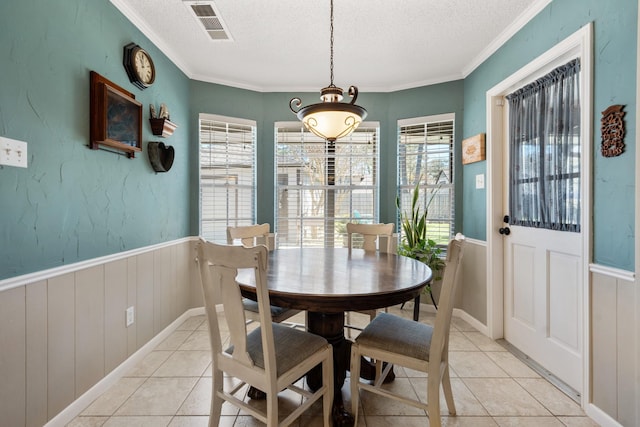 dining area with a textured ceiling, light tile patterned floors, a wainscoted wall, visible vents, and crown molding