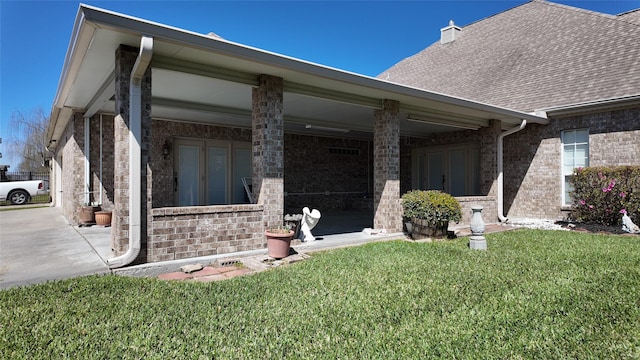 exterior space featuring a shingled roof, brick siding, and a lawn