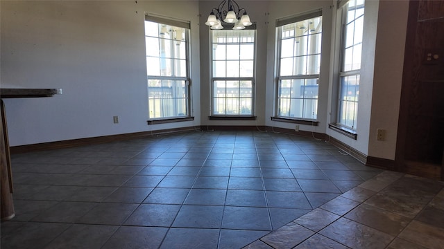 unfurnished dining area featuring a notable chandelier, dark tile patterned floors, and baseboards