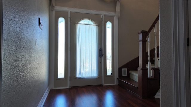 foyer entrance with a textured wall, stairway, and wood finished floors