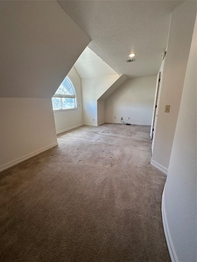 additional living space featuring visible vents, baseboards, lofted ceiling, a textured ceiling, and carpet floors