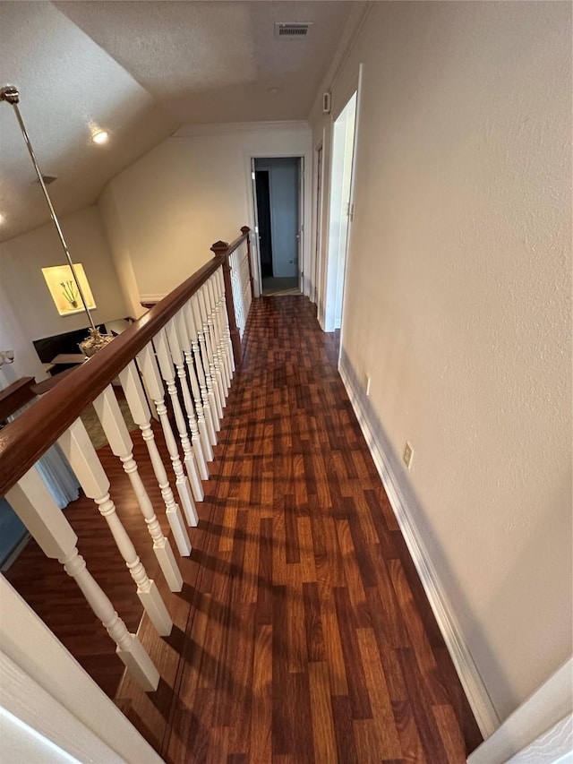 hall featuring baseboards, visible vents, dark wood-style floors, vaulted ceiling, and an upstairs landing