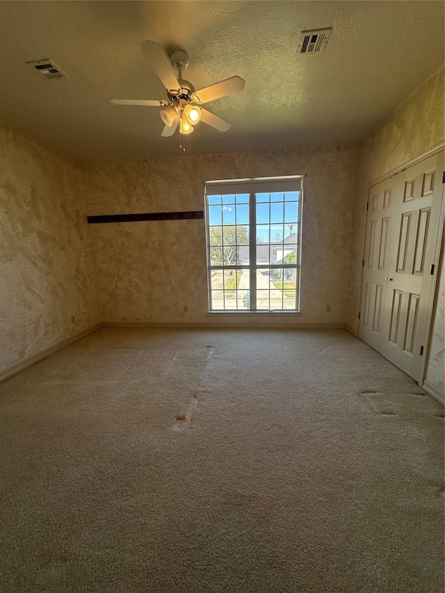 carpeted spare room with a textured ceiling, ceiling fan, and visible vents